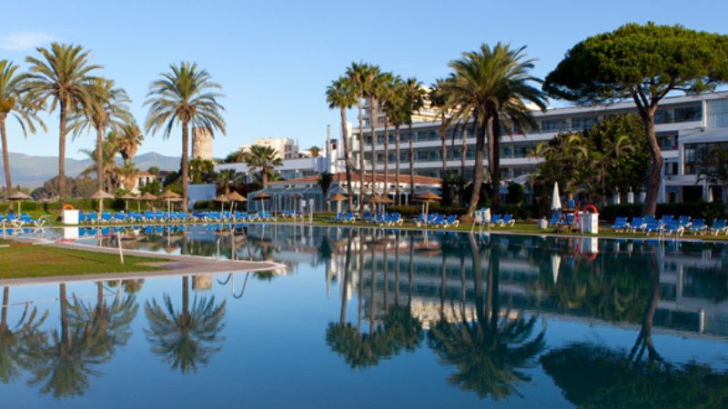 Hotellpool med palmer, solstolar och speglingar i vattnet i Guadalmina.